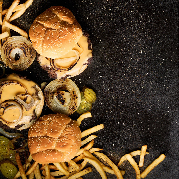 Smash burgers, fries, pickles, and onions on a griddle.