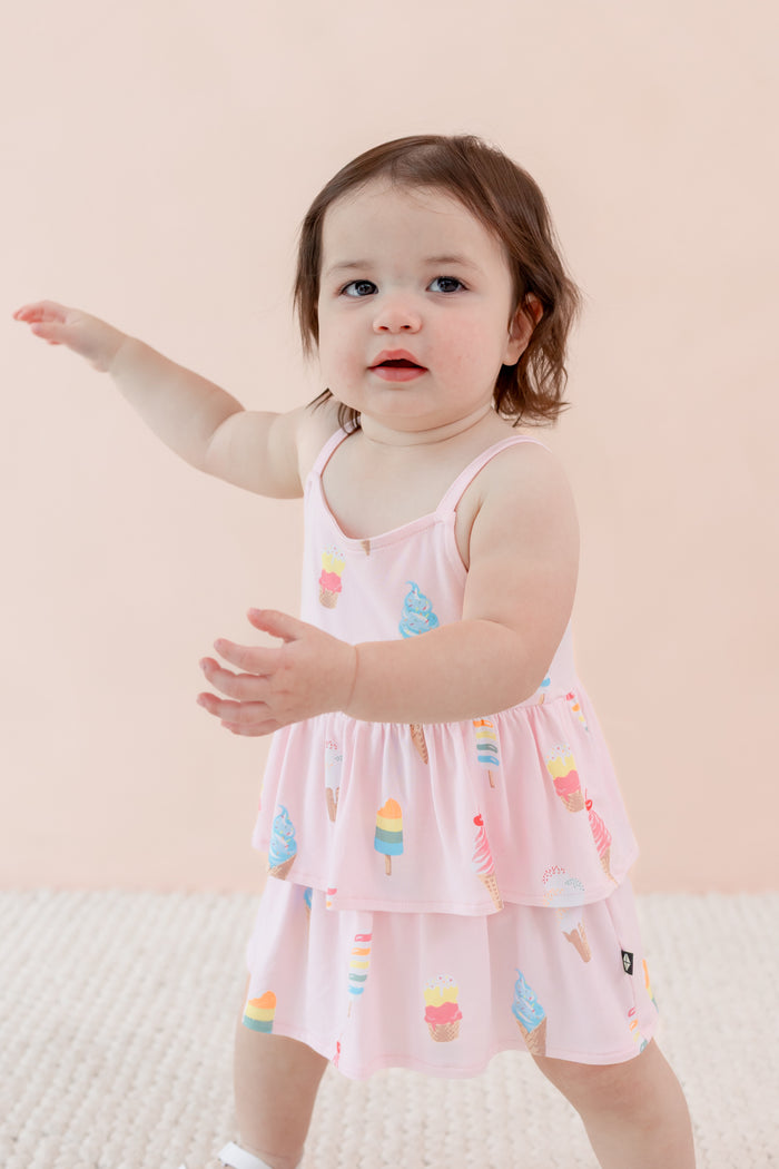 Child posing in spaghetti strap ruffle romper in Sakura Ice Cream print on a beige background