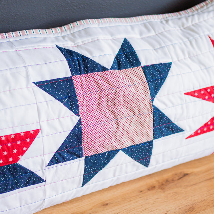 Quilt with star patterns in red, white, and blue on a wooden surface.