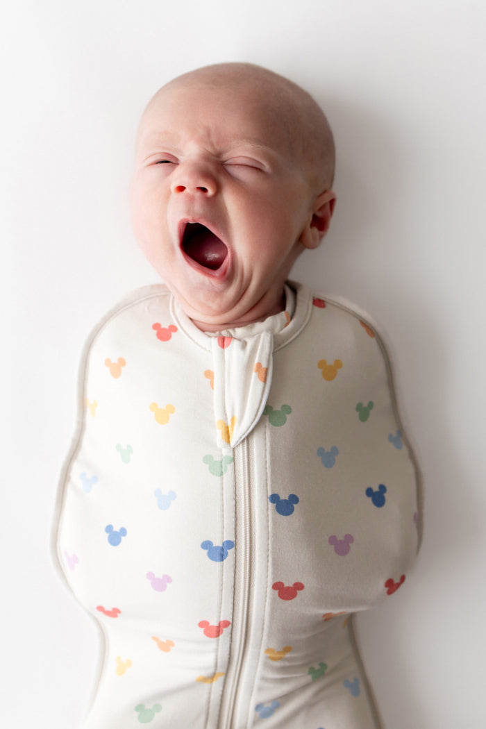 Baby wearing a colorful patterned swaddle yawning on a white background