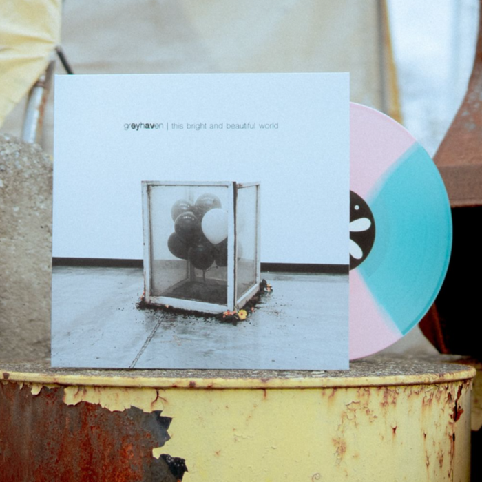 A Greyhaven Sea Blue/Pink Quad Vinyl LP sits behind its album cover—black balloons in a glass box on concrete. Both rest on a rusty yellow barrel outdoors. Full Album Digital Download included with purchase.