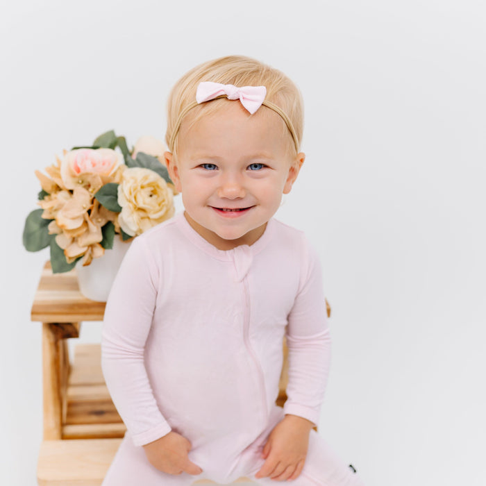 Infant wearing Kyte Baby Tiny Bow with Nylon Band in Sakura pink