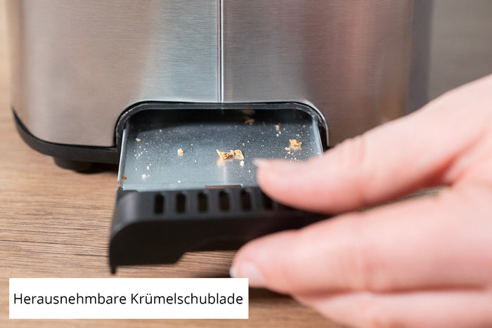 Eine Hand entnimmt die kleine Krümelschublade aus Metall mit Brotkrümeln aus dem Unold Toaster Thommy. Die deutsche Aufschrift lautet „Herausnehmbare Krümelschublade“.