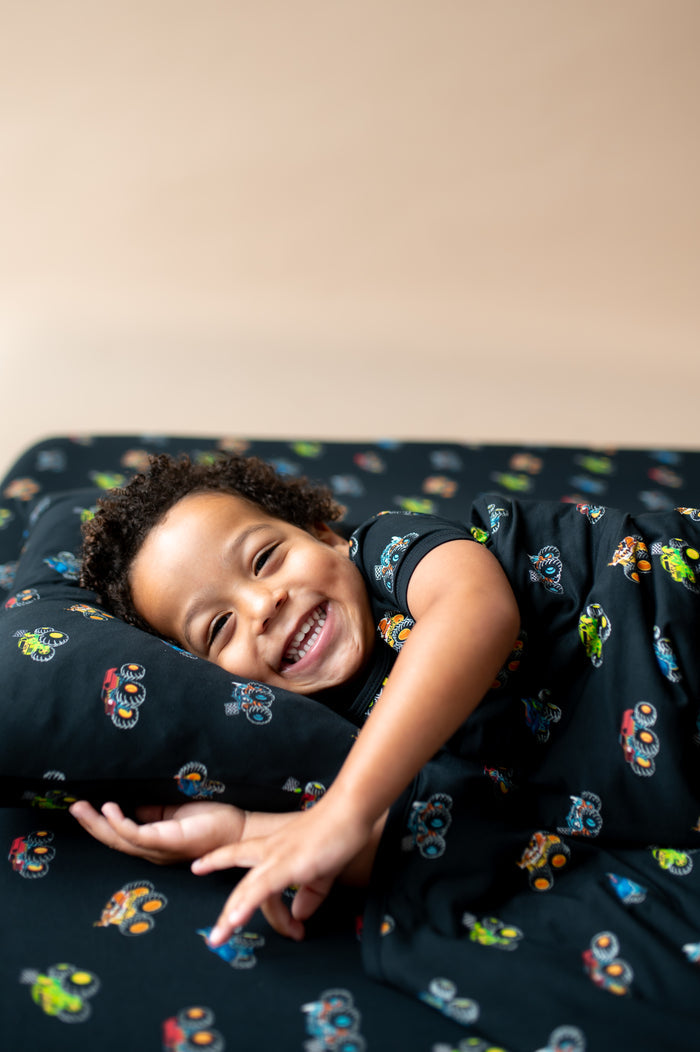 Boy lying on black Toddler pillowcase  and sheet in Monster Truck print covered with a similar print sheet.