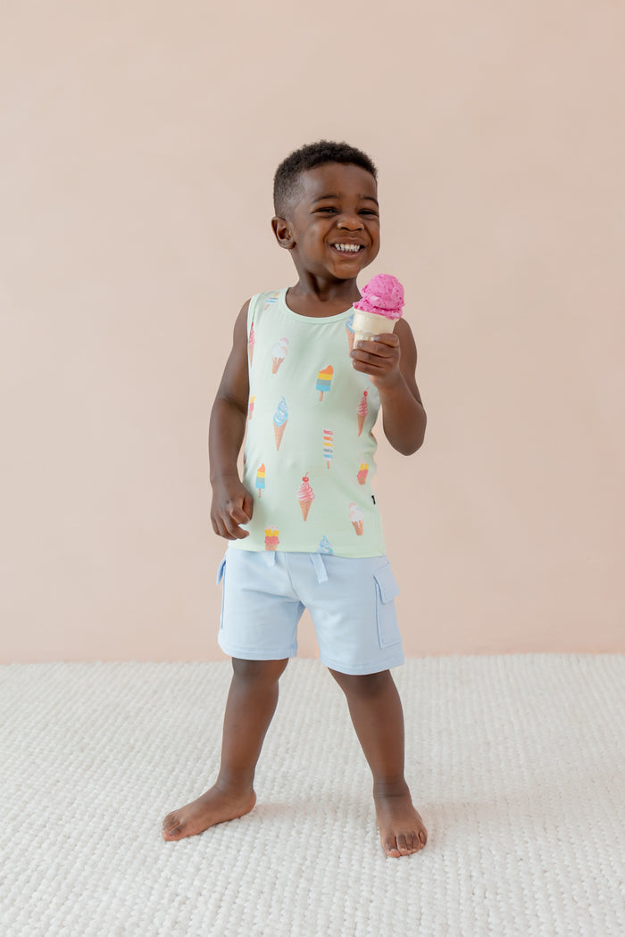 Child smiling and holding an ice cream cone wearing a Toddler Tank Top in Mint Ice Cream print over blue shorts on a beige background