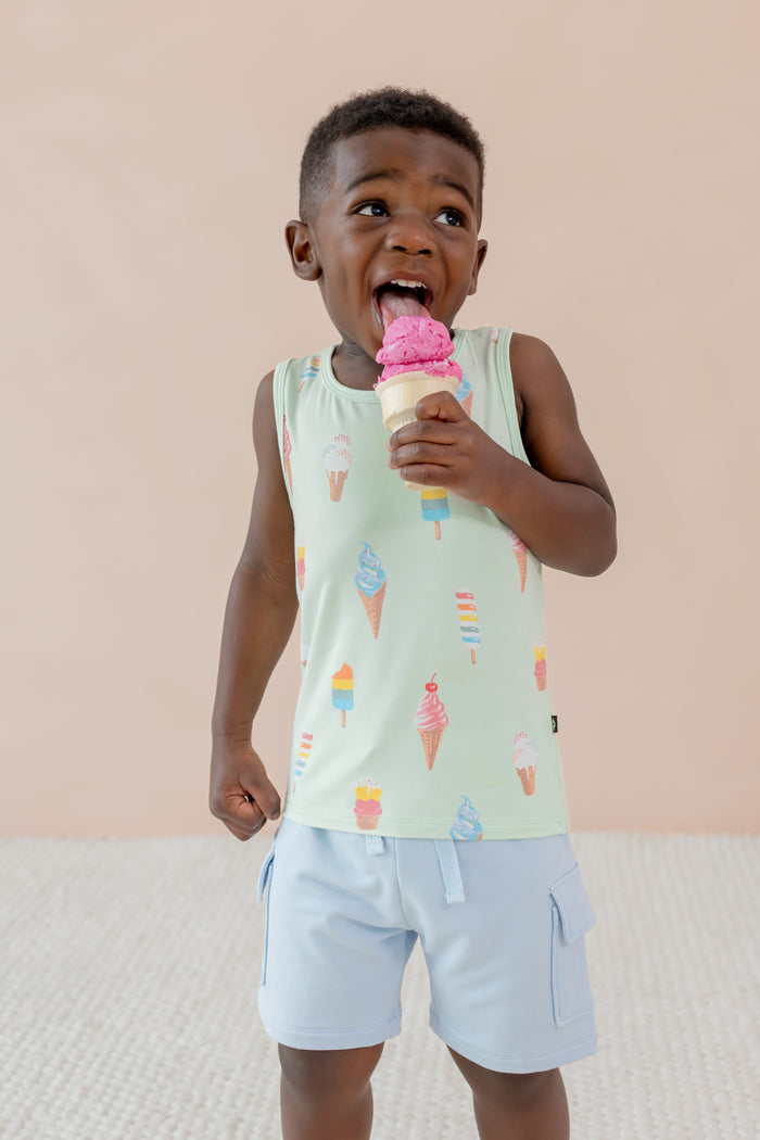 Child eating an ice cream cone wearing a Toddler Tank Top in Mint Ice Cream print over blue shorts on a beige background