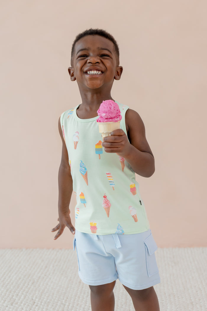 Child posing with an ice cream cone wearing a Toddler Tank Top in Mint Ice Cream print over blue shorts on a beige background