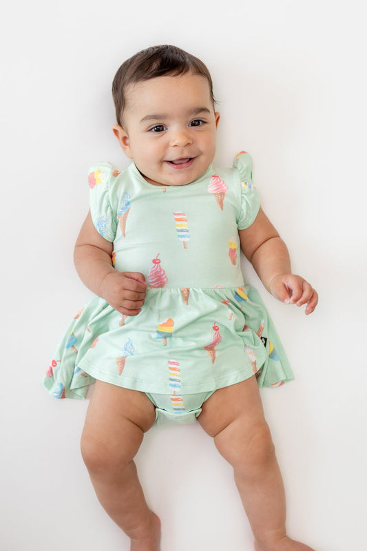 Baby wearing Twirl Bodysuit Dress in Mint Ice Cream print on a beige background