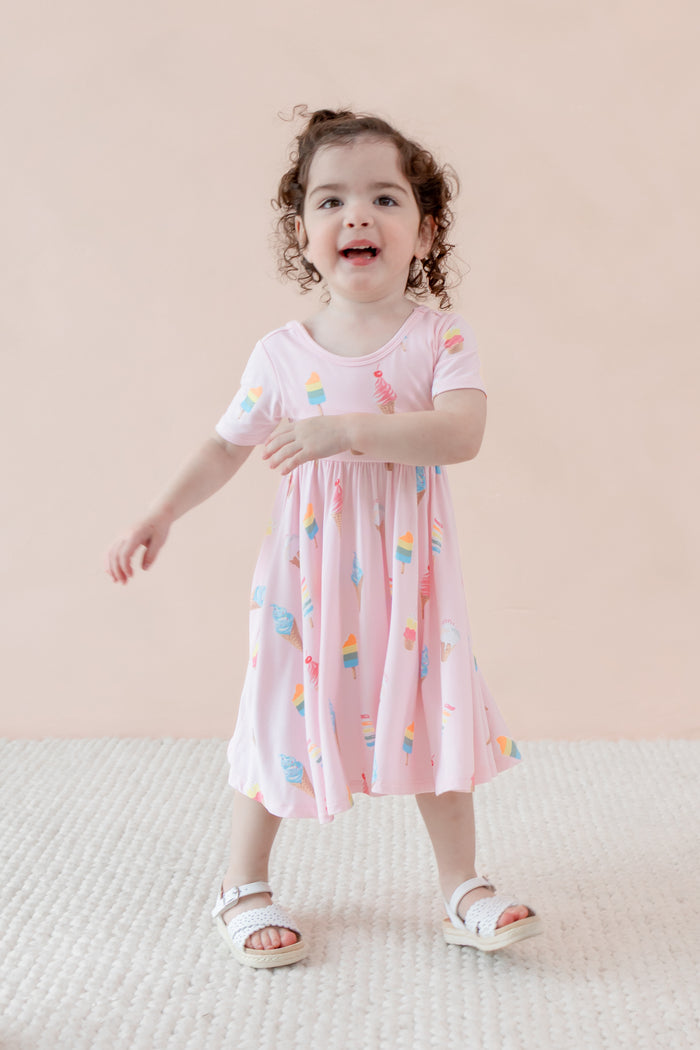 Child posing in Twirl Dress with Sakura Ice Cream print wearing sandles on a beige background