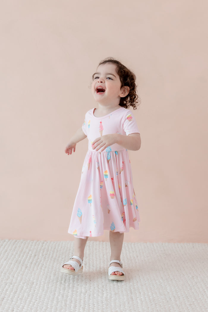 Child laughing in Twirl Dress in Sakura Ice Cream print with sandles on a beige background