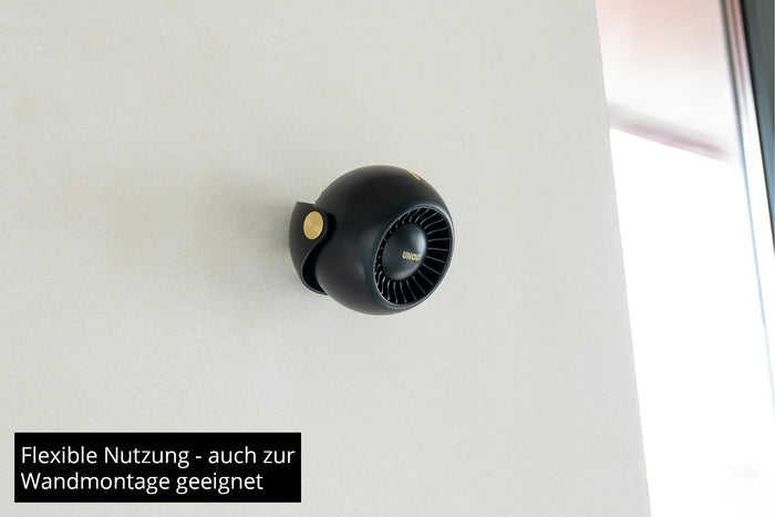 Eine kleine, schwarze Ventilator Breezy Bowl von Unold ist an einer weißen Wand montiert. Der deutsche Text darunter lautet: Flexible Nutzung – auch zur Wandmontage geeignet.