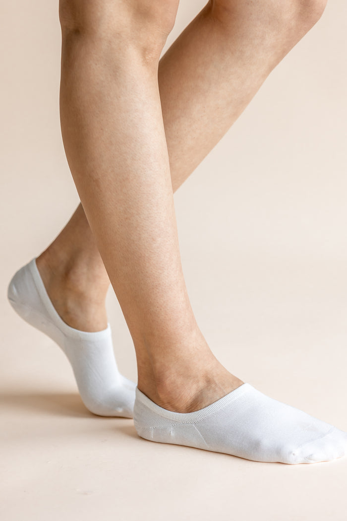 White low-cut no-show socks worn on a person's feet, shown against a solid light beige background.