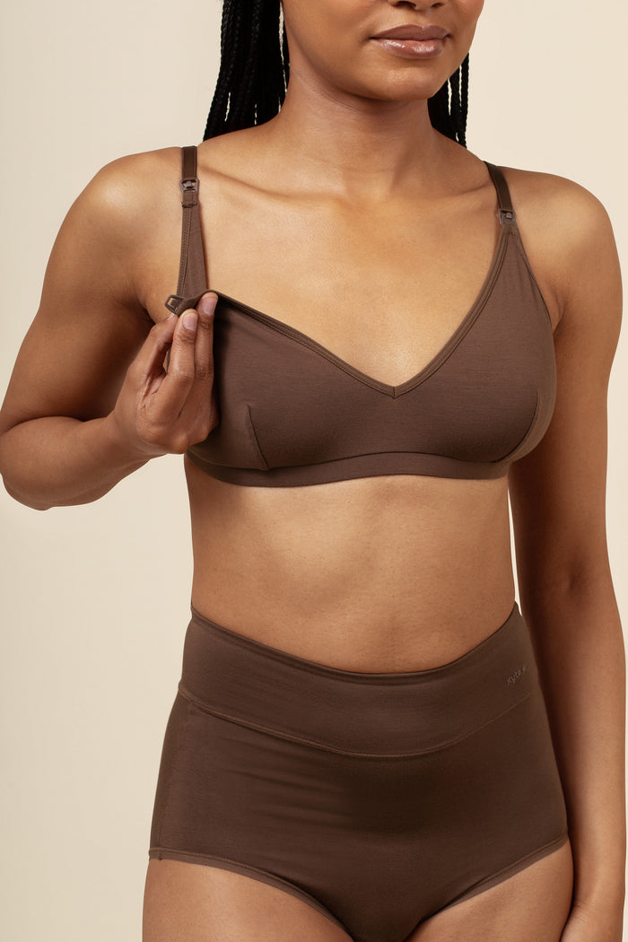 Woman wearing a brown nursing bra with clasp for easy nursing and panties set against a beige background