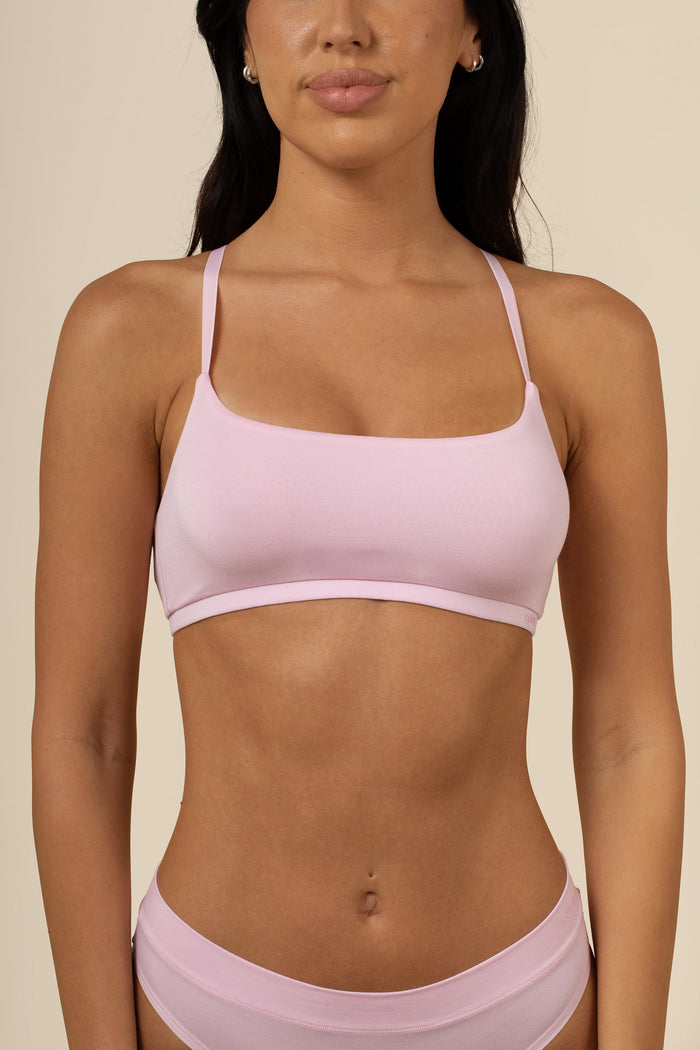 Woman wearing a pink scoop bra and shorts on a beige background
