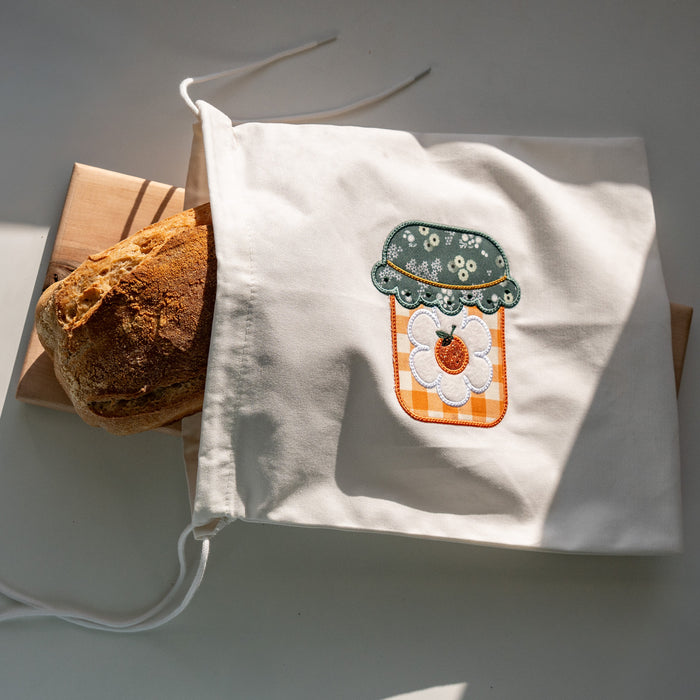 White tote bag with a design of a potted plant and pumpkin on a gray surface.