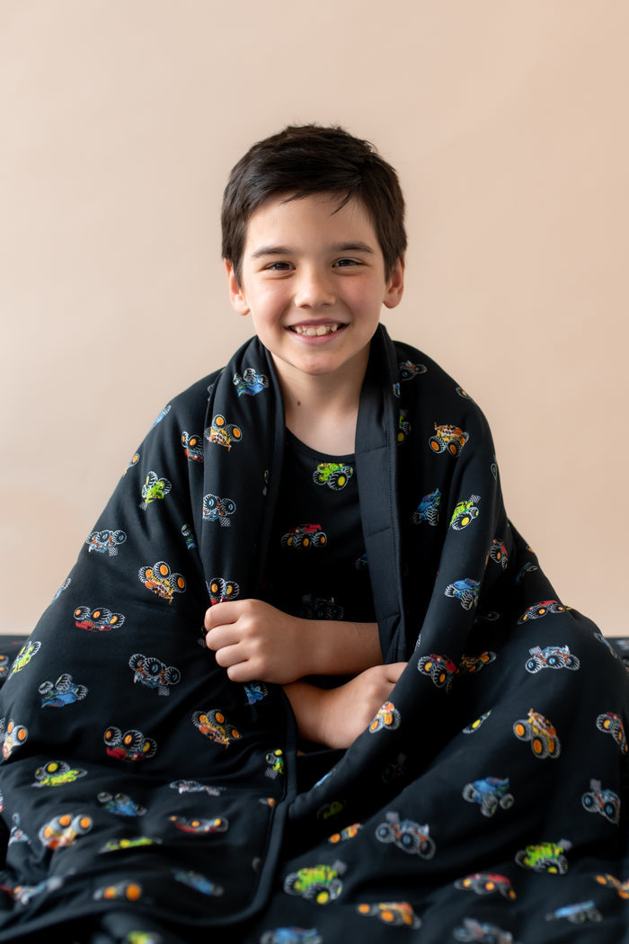 Boy smiling wrapped in black Youth Blanket in Monster Truck print on a beige background