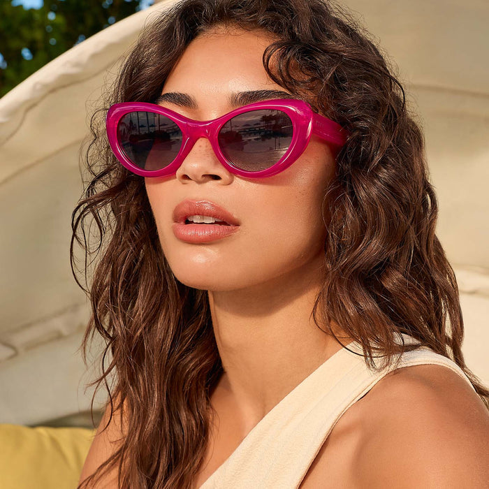 lifestyle - female on a day bed wearing diff eyewear zaria cat eye sunglasses with a bright tulip pink frame and grey gradient polarized lenses
