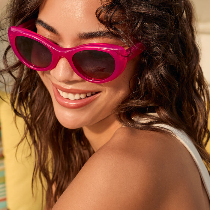 lifestyle - female on a day bed wearing diff eyewear zaria cat eye sunglasses with a bright tulip pink frame and grey gradient polarized lenses close up view