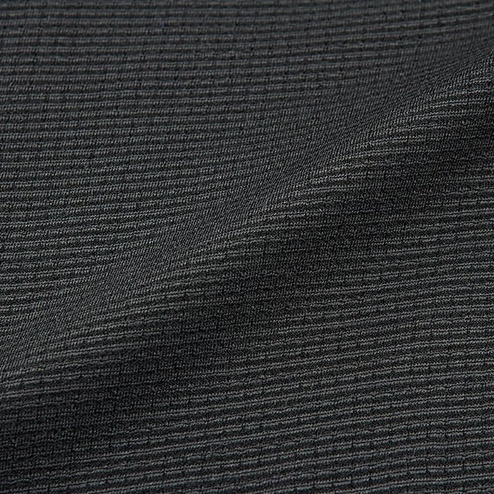 A textured dark fabric lies in folds showcasing a series of fine, parallel ridges creating a subtle pattern against a neutral backdrop suggesting clothing or upholstery fabric in a softer light setting
