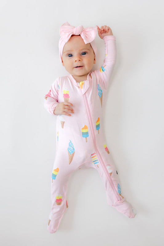 Baby wearing Zippered footie in Sakura Ice cream print with pink bow headband on a white background