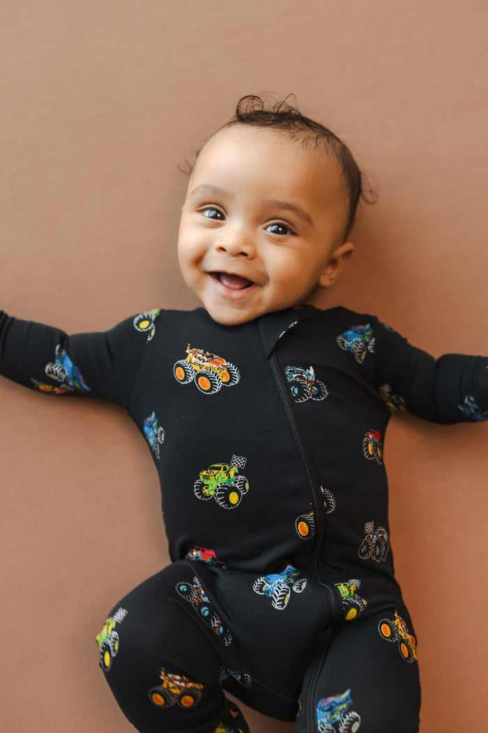 Baby smiling in black Zippered Romper in Monster Truck print on beige background